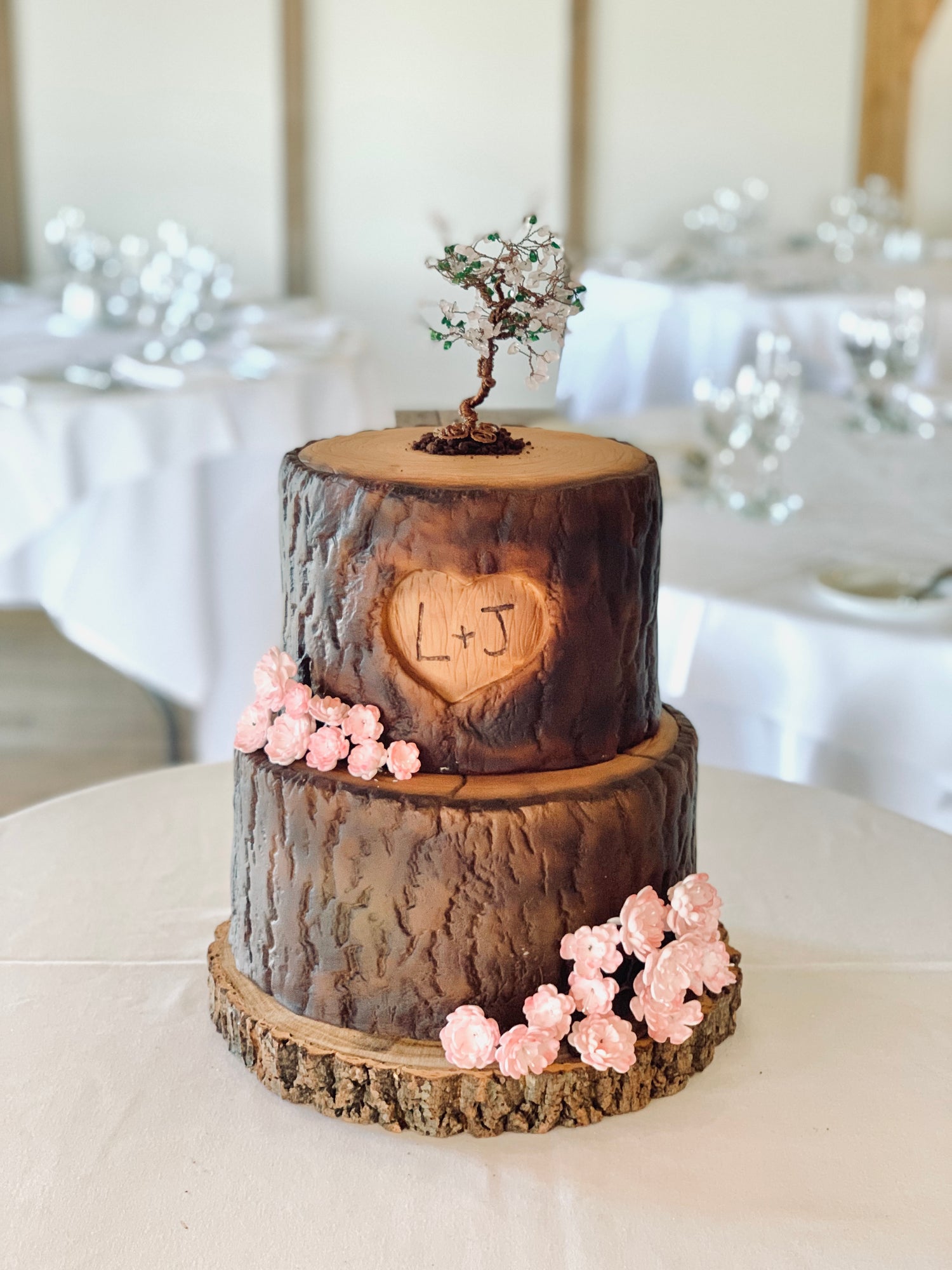 Two-tiered tree trunk affect cake with floral decorations on a table.